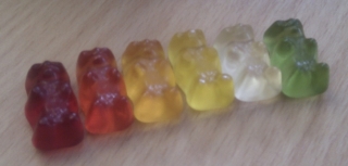 Row of gummi bears with colours in the following order: dark red, red, orange, yellow, white, green